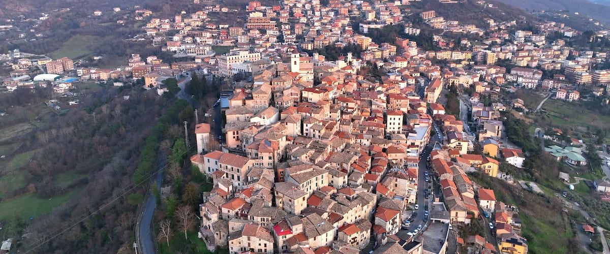 A densely packed town with red-roofed buildings, surrounded by hills and a river.