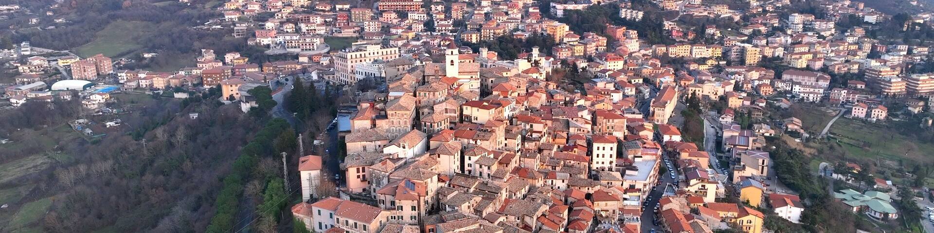 A densely packed town with red-roofed buildings, surrounded by hills and a river.