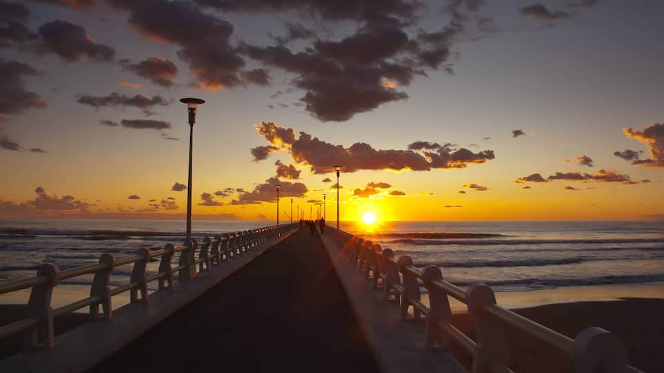 A sunset over the ocean with a pier extending into the water.