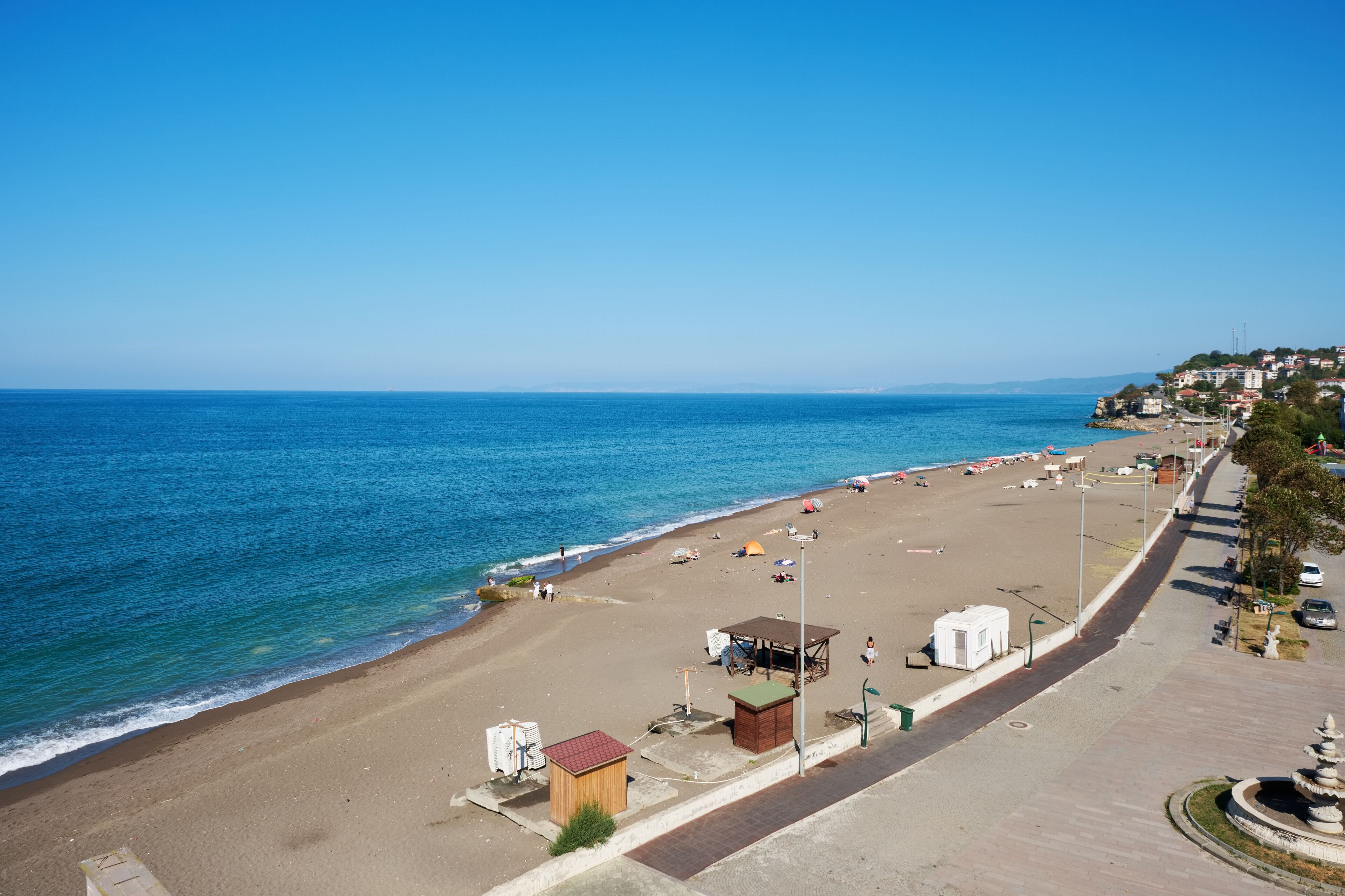 Una playa con cielo despejado, orilla arenosa, algunos edificios y una carretera aledaña.