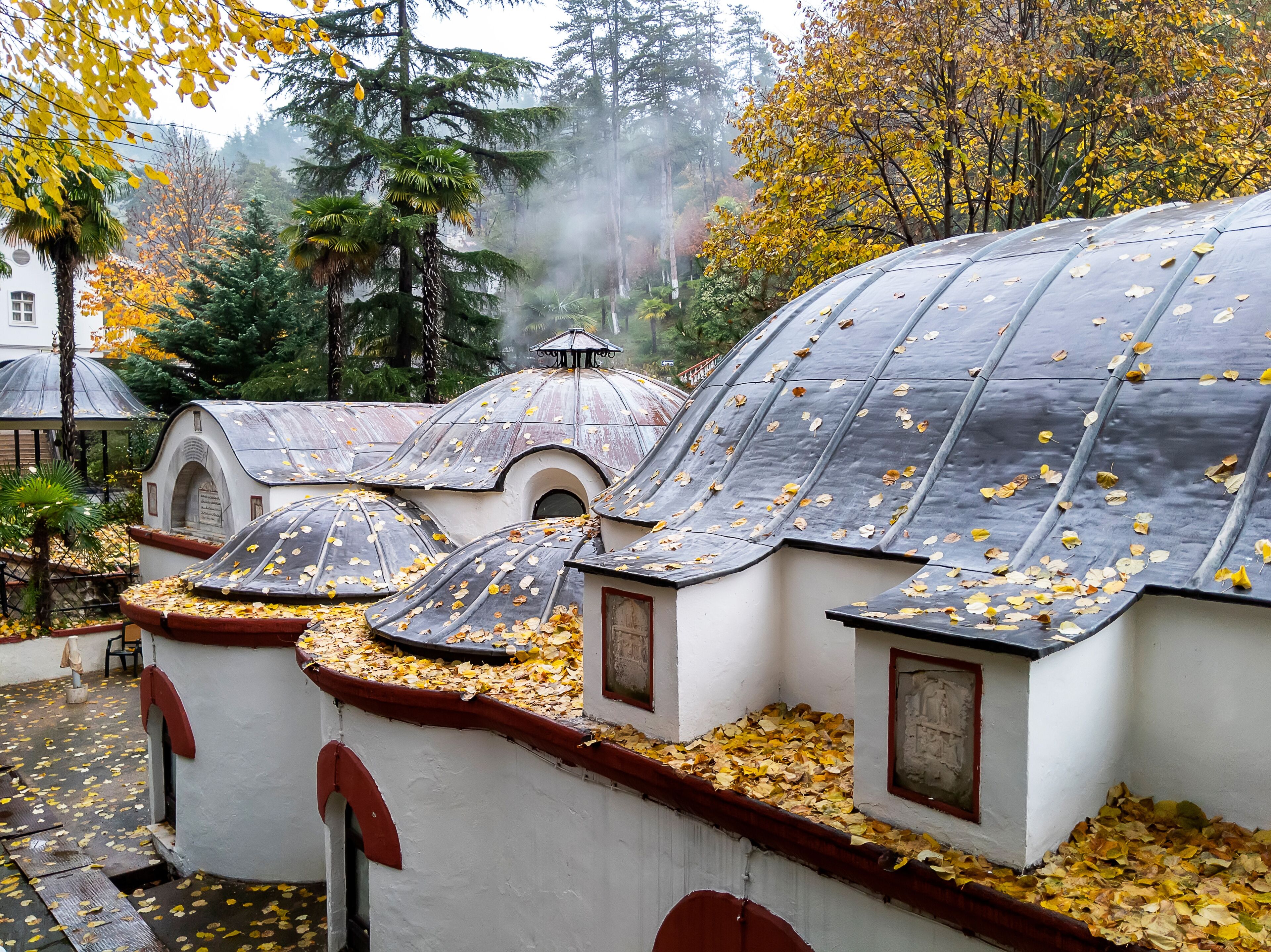 Un jardín con edificios blancos y techos abovedados cubiertos de hojas otoñales.
