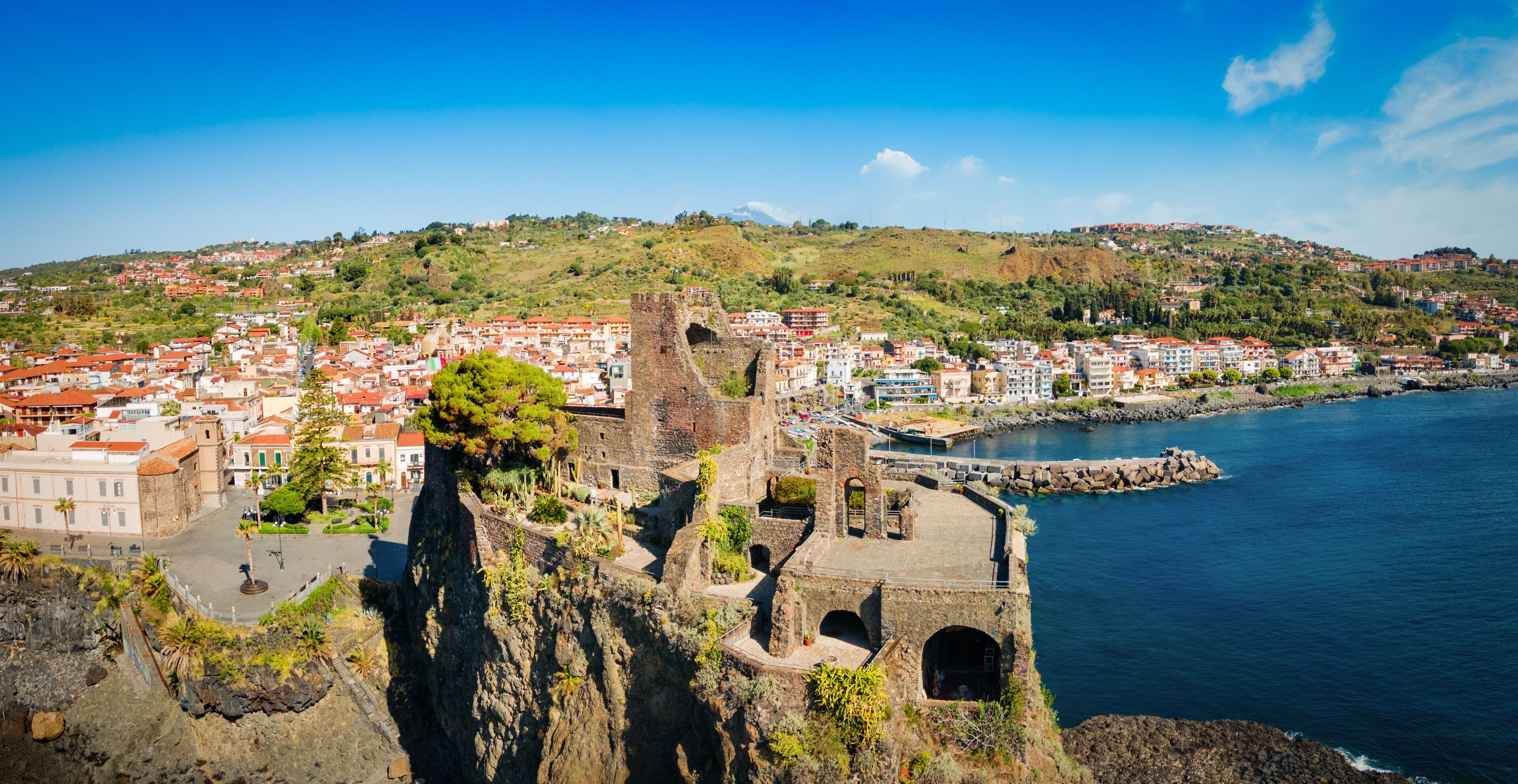 A coastal town with a historic fort overlooking the sea, surrounded by residential buildings and a hilly landscape.