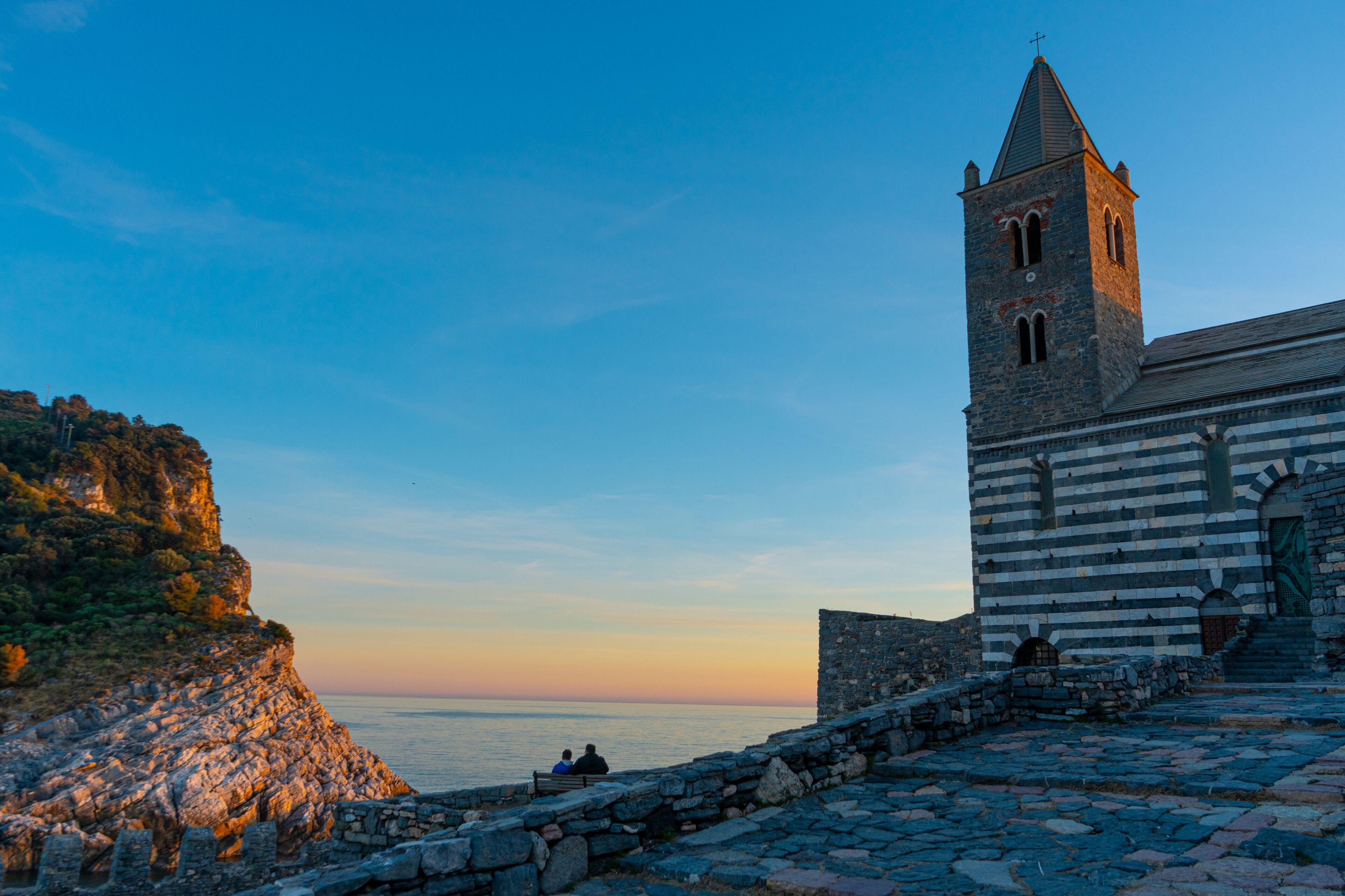 A coastal church with a bell tower, stone steps, and a view of the sea.