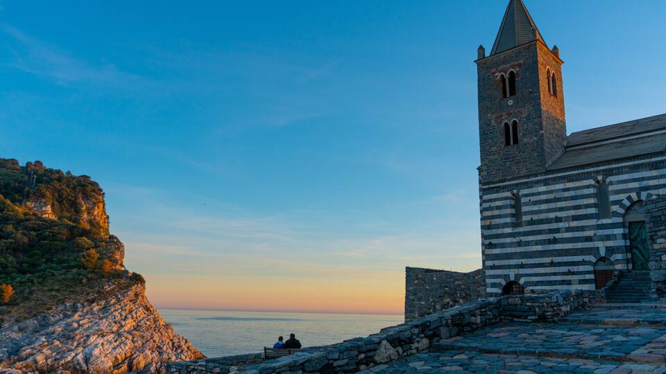 A coastal church with a bell tower, stone steps, and a view of the sea.