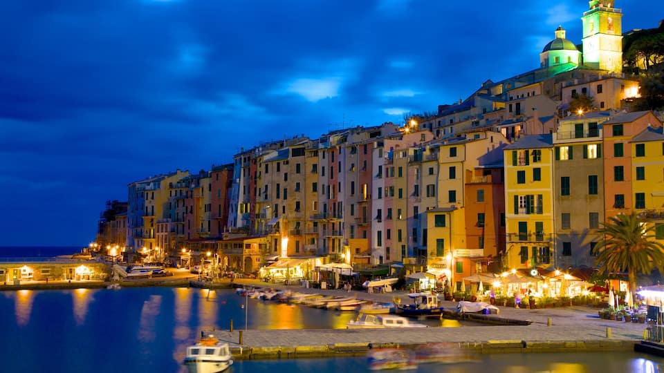A waterfront cityscape at night with colorful buildings, a prominent church tower, and boats docked along the quay.