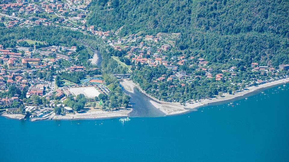 An aerial view of a coastal town with a dense cluster of buildings, a narrow road leading to the sea, and a beach with boats.