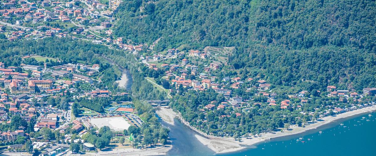 An aerial view of a coastal town with a dense cluster of buildings, a narrow road leading into the town, and a beach area with boats.