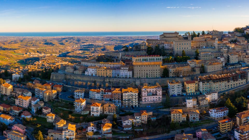 A historic city with a prominent castle on a hill, surrounded by residential buildings and a coastal view.