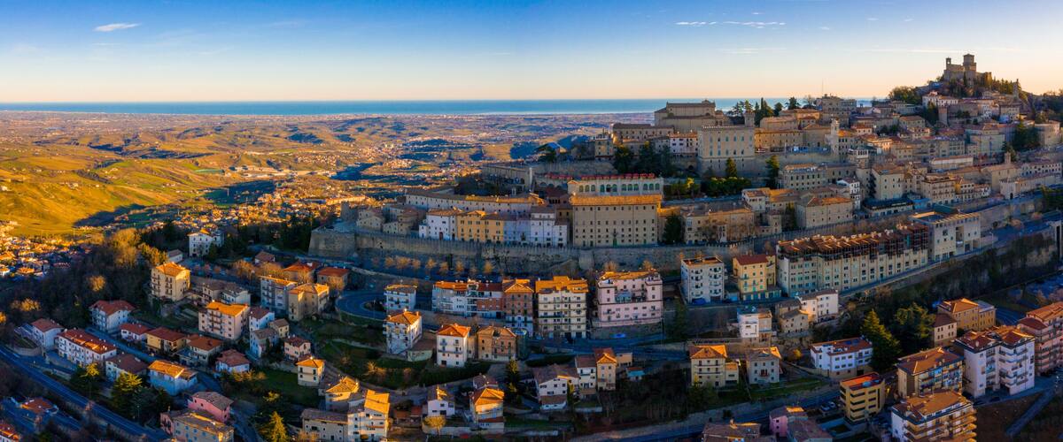 A historic city with a prominent castle on a hill, surrounded by residential buildings and a coastal view.