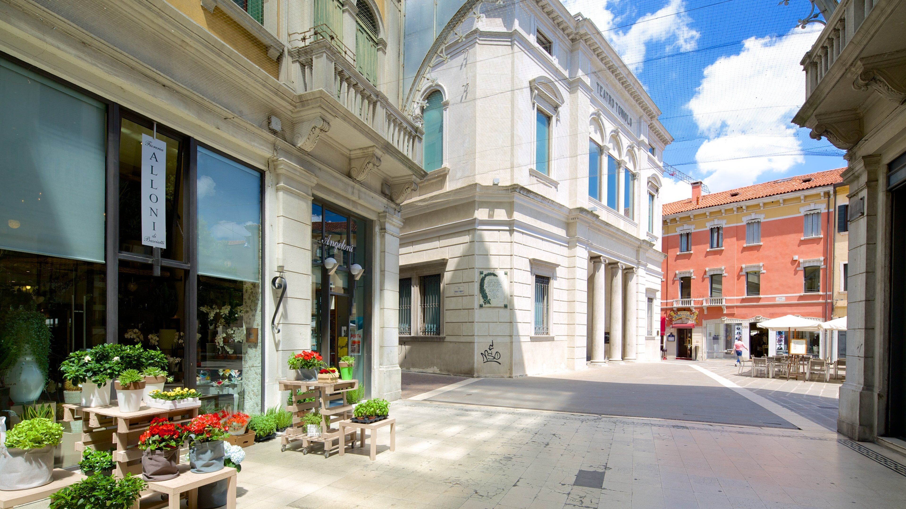 A street with a flower shop, a building with a sign reading "Teatro Tonino", and a red building in the background.