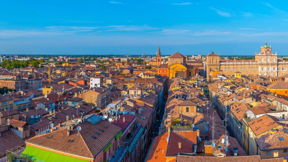 A panoramic view of a historic city with dense architecture, including a prominent church with a dome and a large cathedral with a green roof.