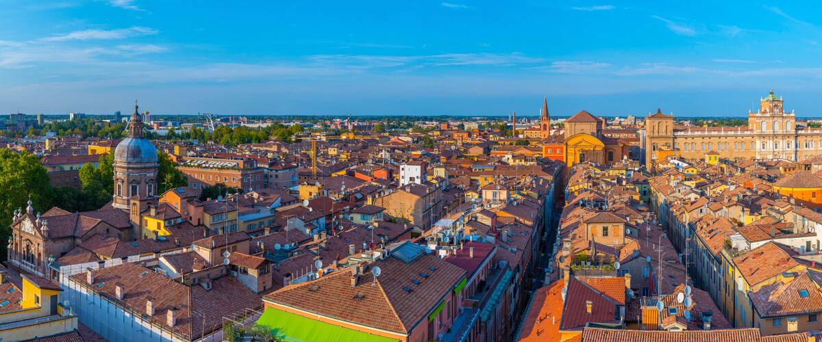 A panoramic view of a historic city with dense architecture, including a prominent church with a dome and a large cathedral with a green roof.