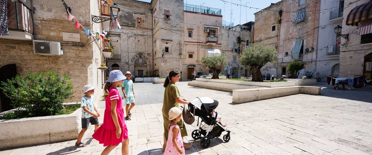 A historic stone square with buildings, a tree, and a stroller.