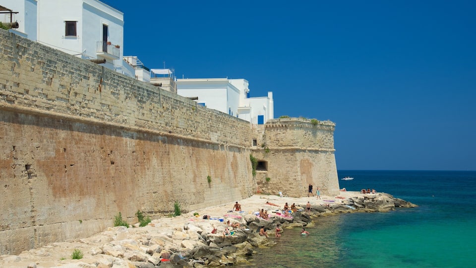 A coastal town with a historic stone wall, white buildings, and clear turquoise waters.