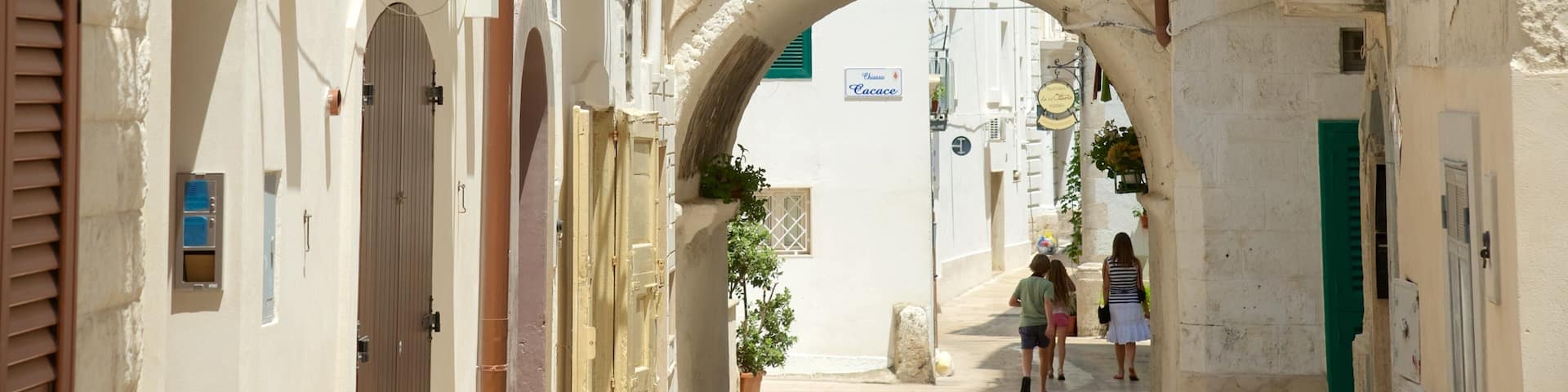 A narrow street with an archway, buildings with shutters, and a sign for 'Cacace'.