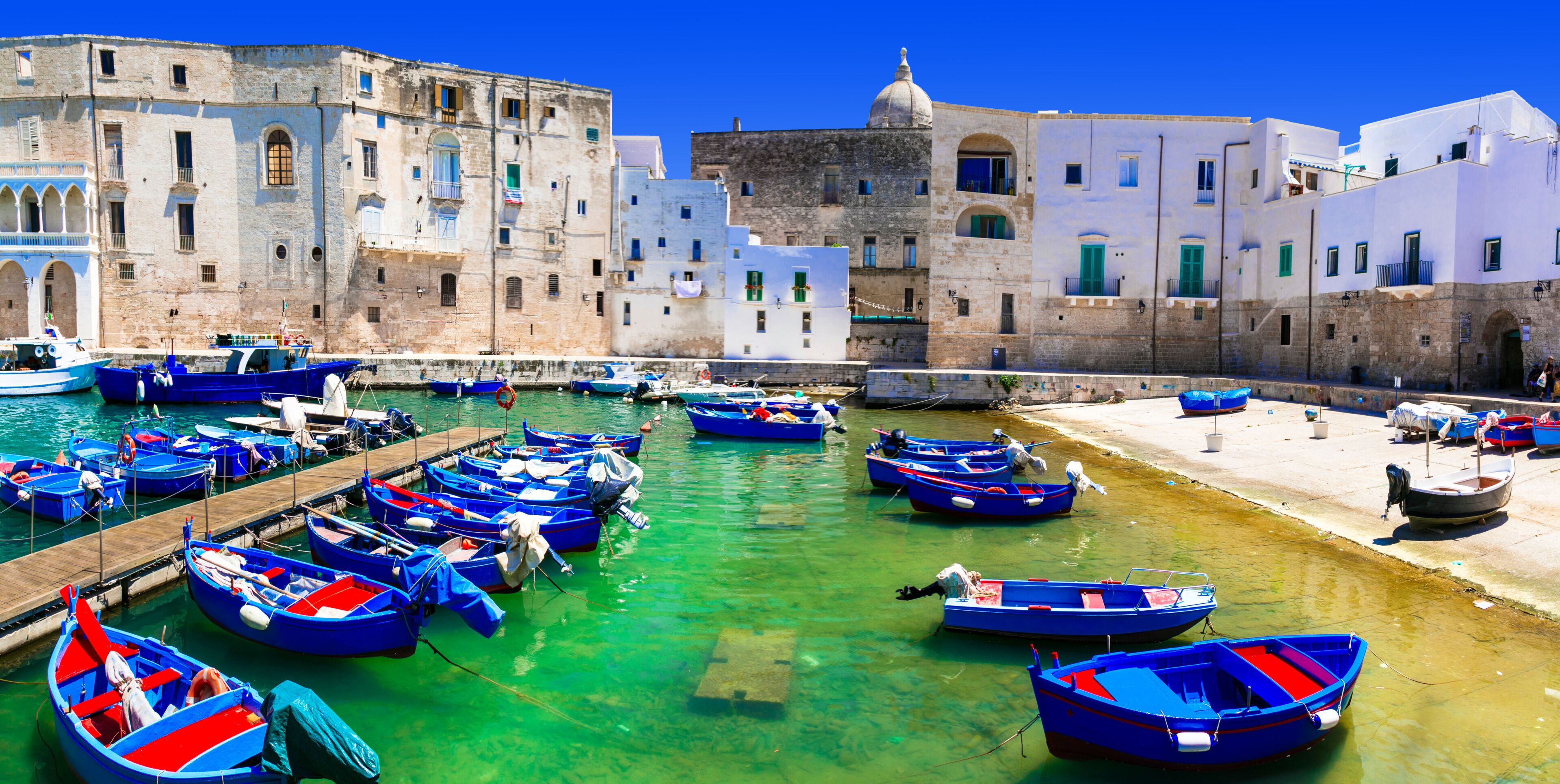 A harbor with numerous small boats docked, surrounded by historic buildings with white and blue facades.