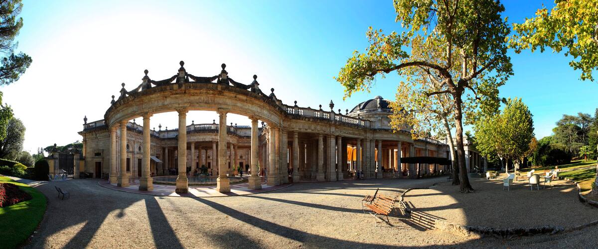 A grand, ornate building with a large archway, surrounded by trees and a well-maintained garden.