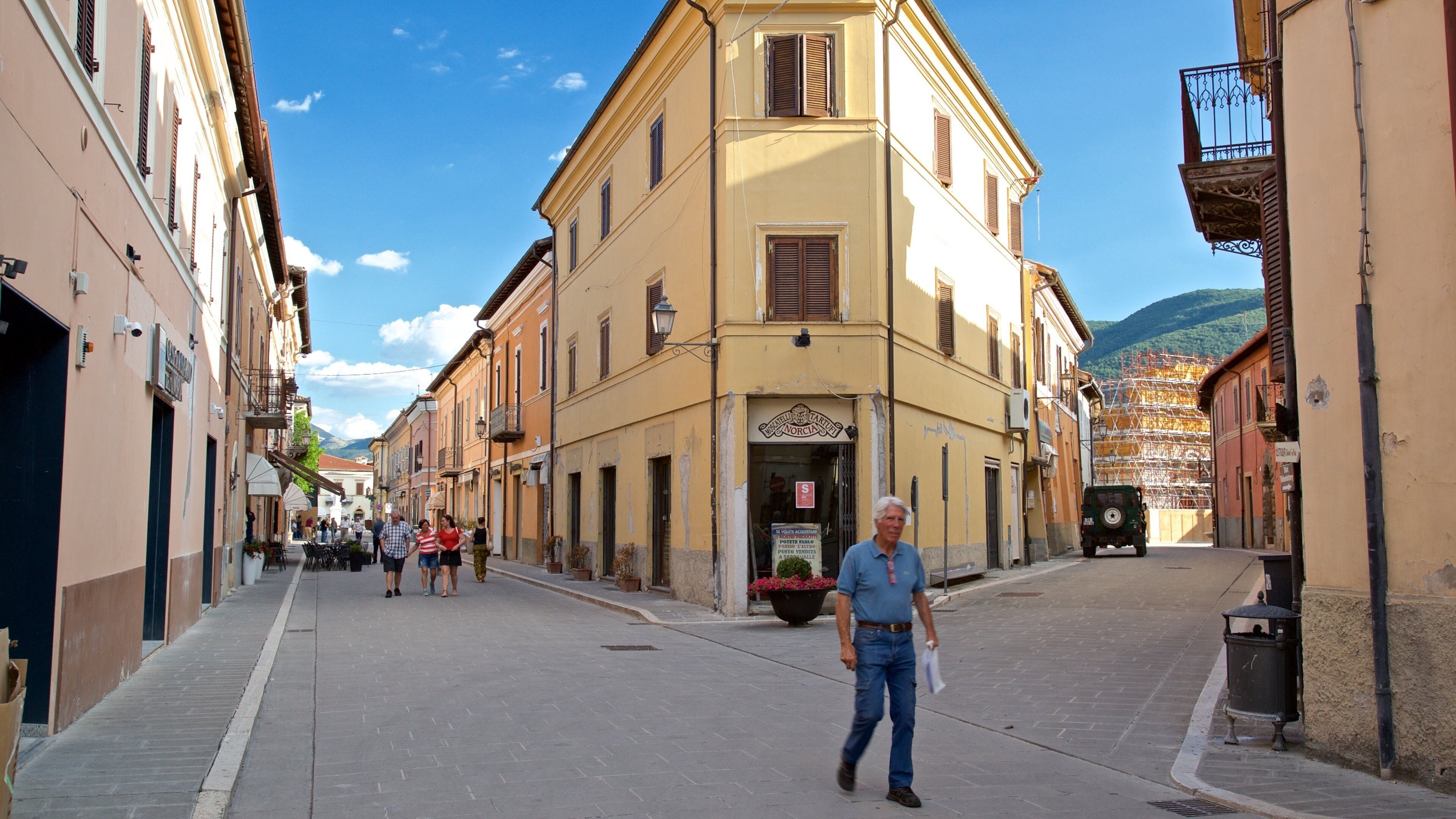 A street in a European town with historic buildings, a man walking, and a parked vehicle.