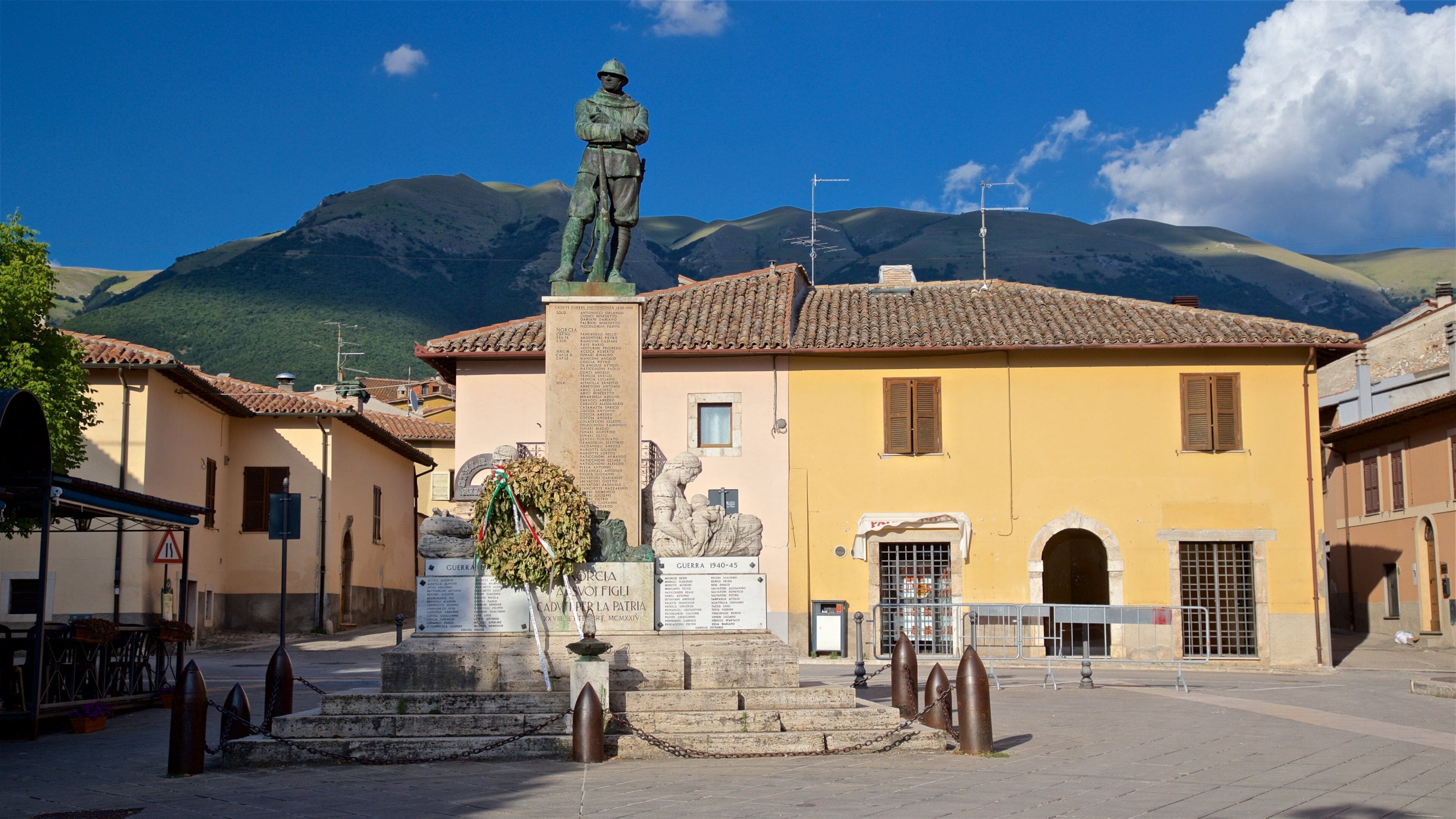A statue of a soldier in a square with a mountain backdrop, surrounded by traditional buildings.