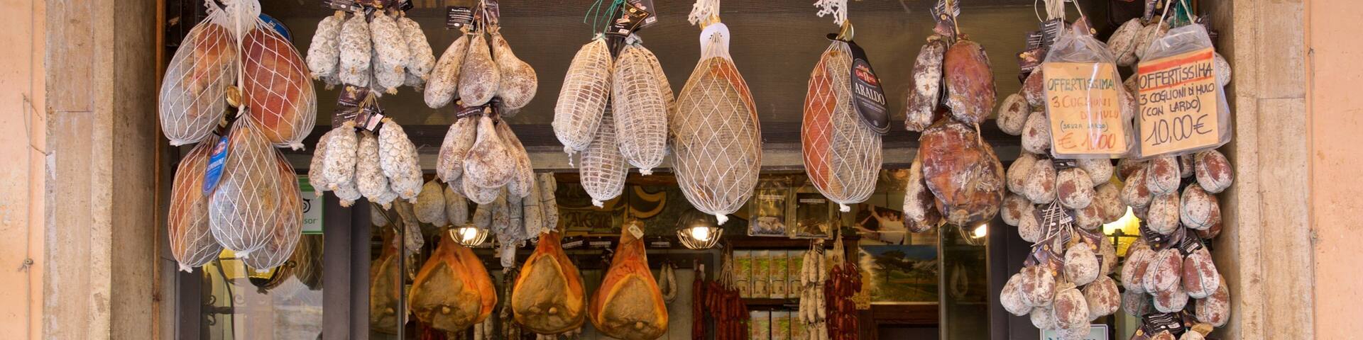 A butcher shop with various meats hanging for sale, including prosciutto and other cured meats.