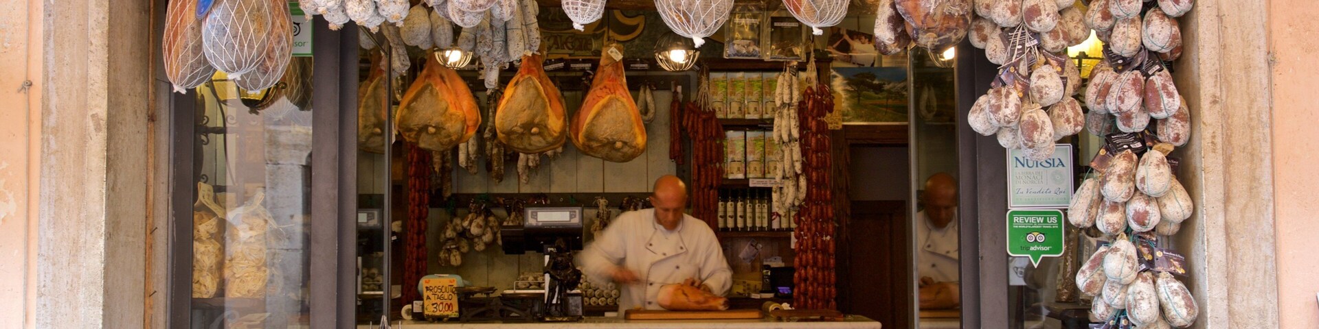 Uma açougue com diversos tipos de carne pendurada à venda, incluindo presunto e outros embutidos.