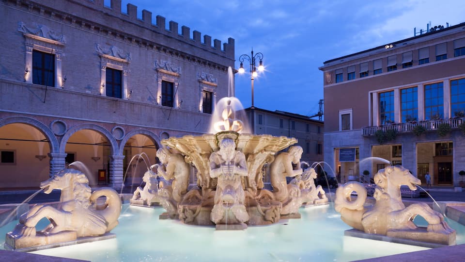 A historic fountain with horses and a central statue in an urban square.