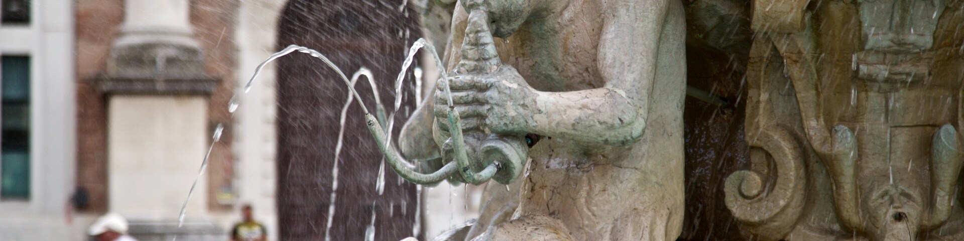A stone fountain with a sculpture of a figure playing a flute, surrounded by water spouts.