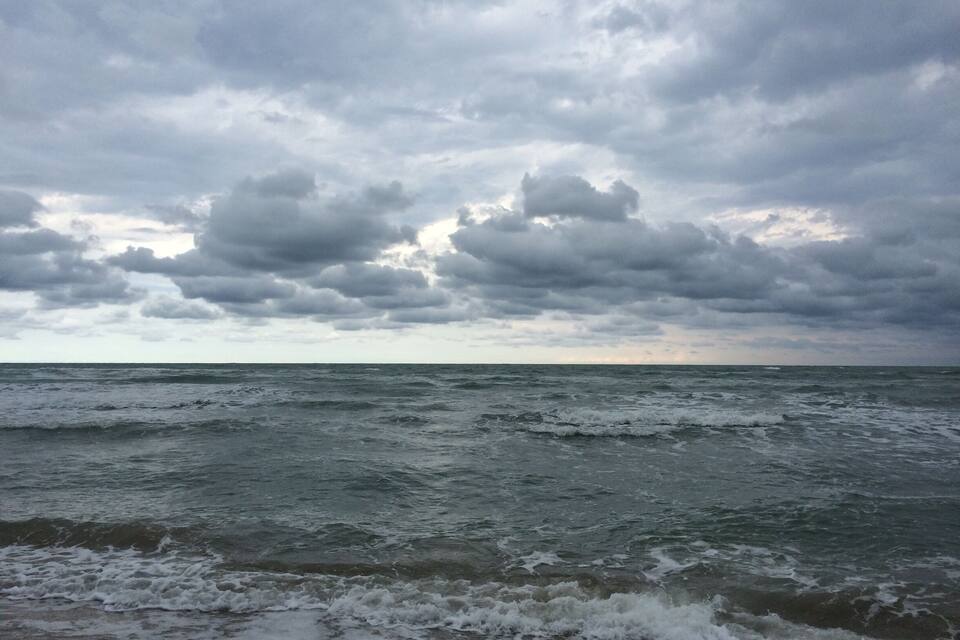 A cloudy sky over the ocean with waves crashing onto the shore.