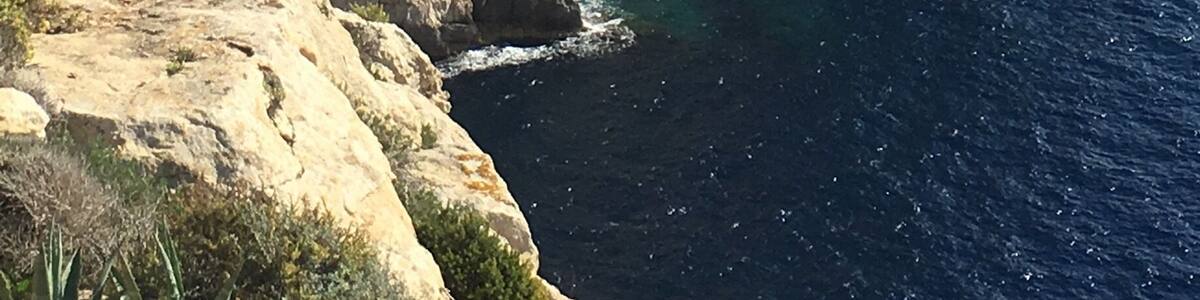 A coastal cliff with layered rock formations and a clear view of the ocean.