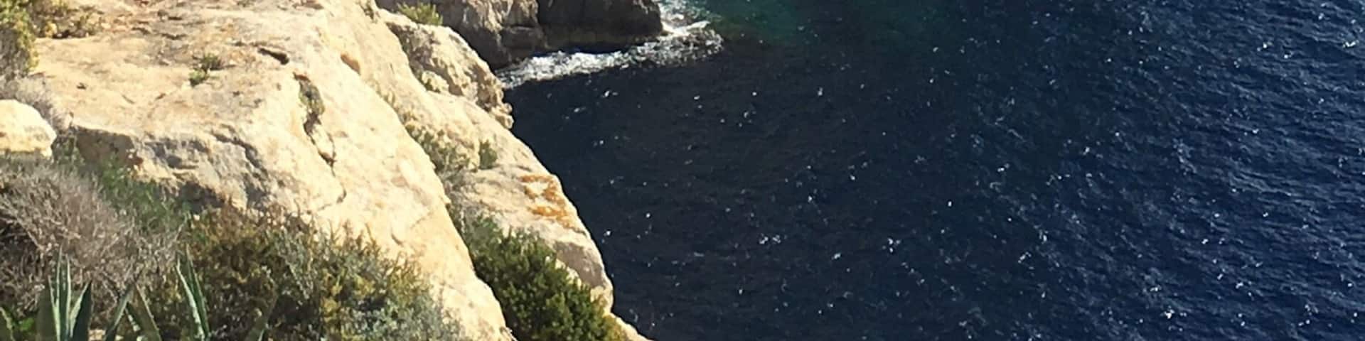 A coastal cliff with layered rock formations and a clear view of the ocean.