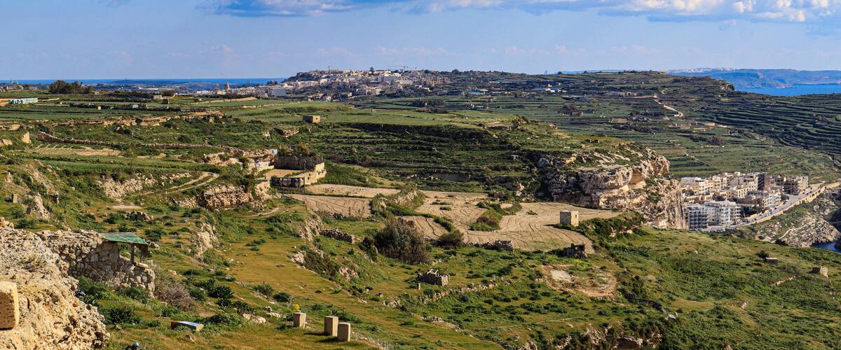 A coastal landscape with terraced fields, ruins, and a distant town.