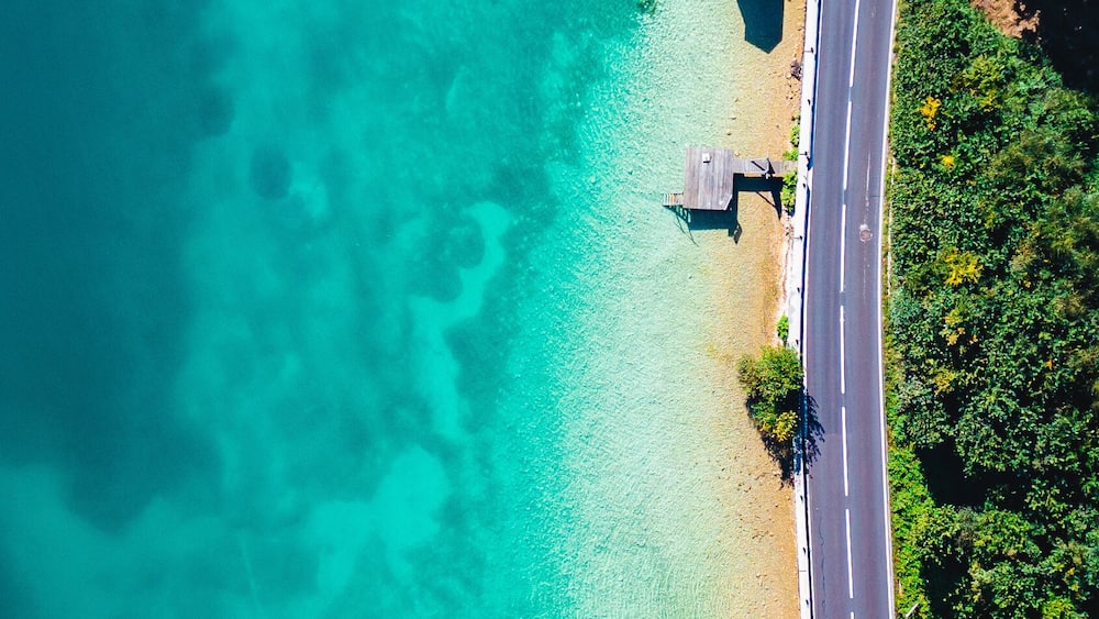 A turquoise beach with clear waters, a paved road, and wooden structures.