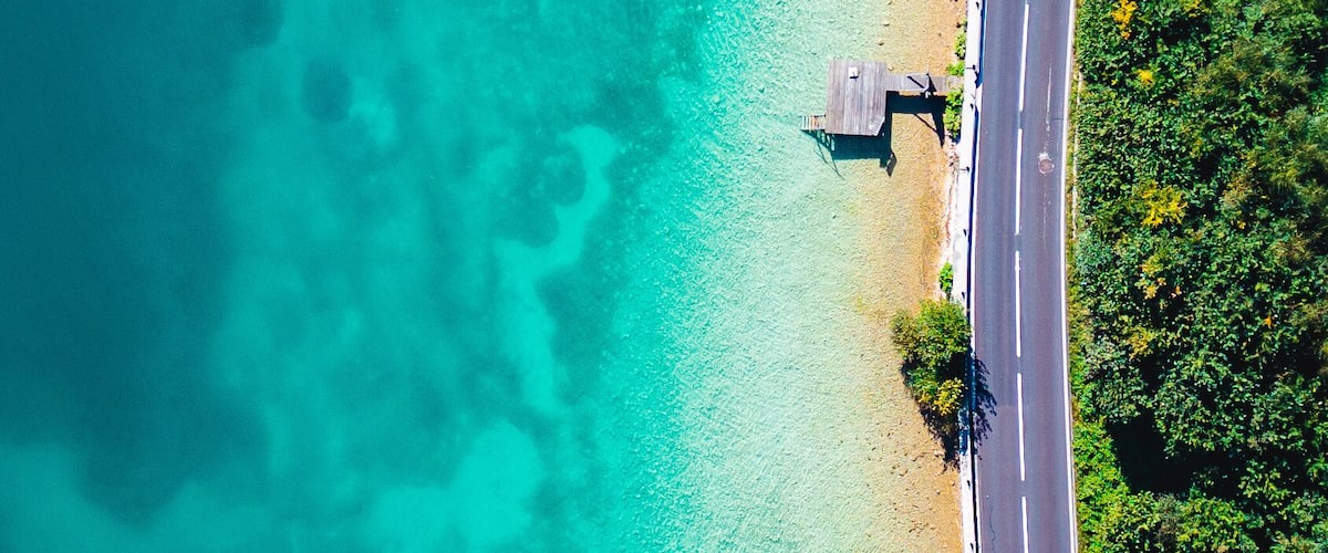 A turquoise beach with clear waters, a paved road, and wooden structures.