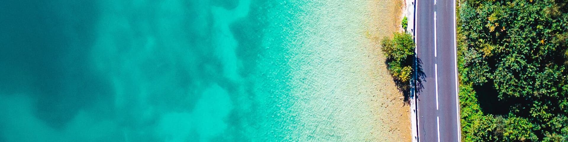 A turquoise beach with clear waters, a paved road, and wooden structures.