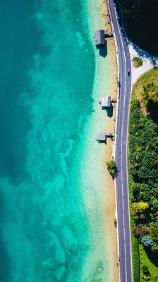 A turquoise beach with clear waters, a paved road, and wooden structures.