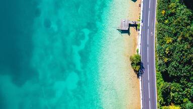 Uma praia turquesa com águas cristalinas, uma estrada pavimentada e estruturas de madeira.
