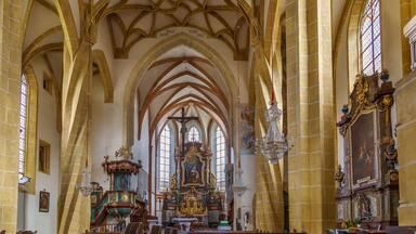A cathedral interior with high vaulted ceilings, stained glass windows, and ornate religious artwork.