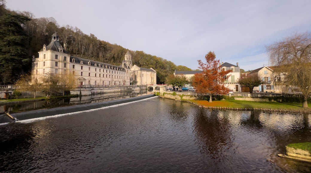 Un río con un puente, un edificio histórico grande y árboles.