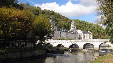 A stone bridge over a river with a historic building and a tower in the background.