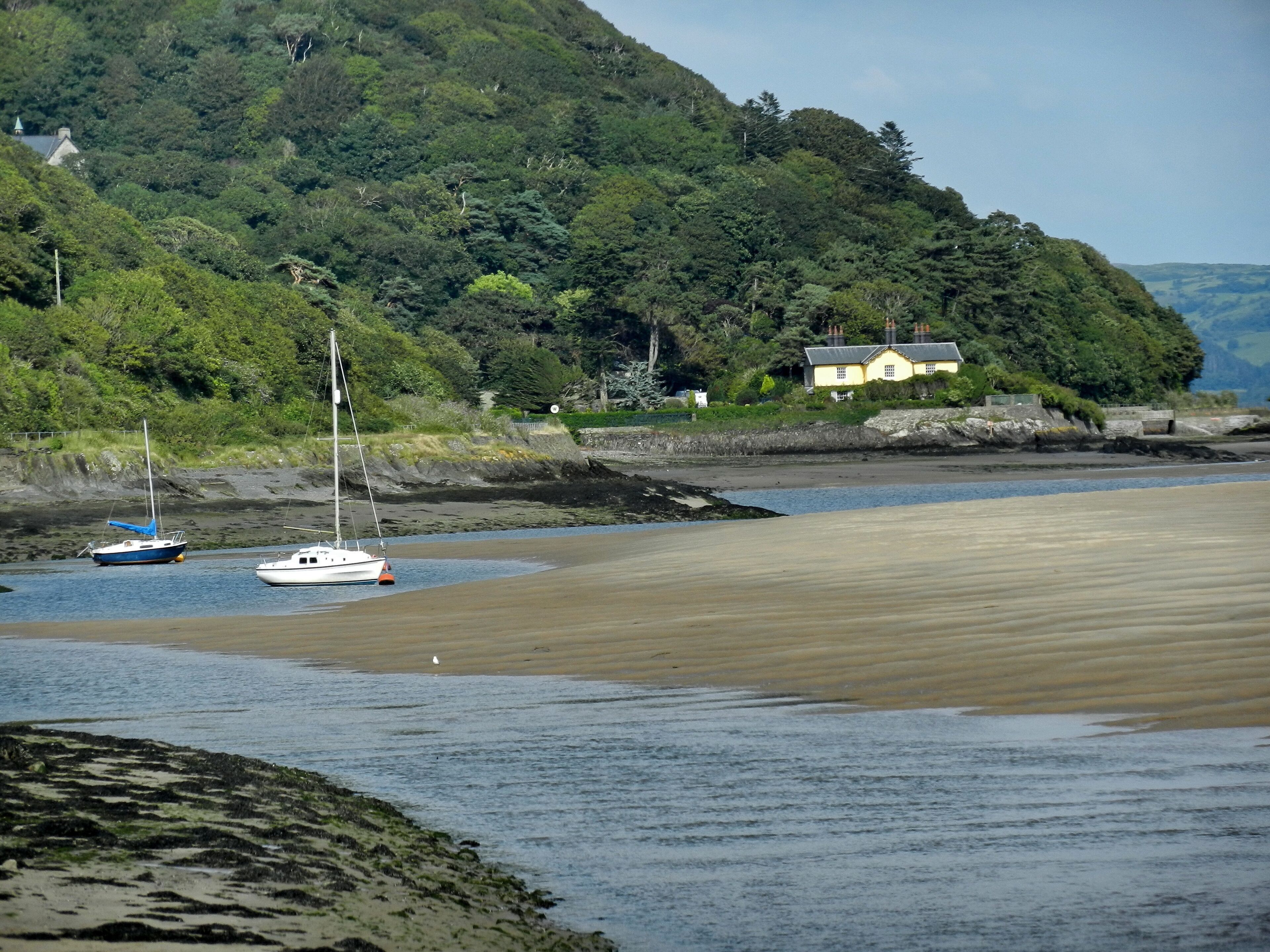 A coastal landscape with a sandy beach, a small boat, and a house on a hill.