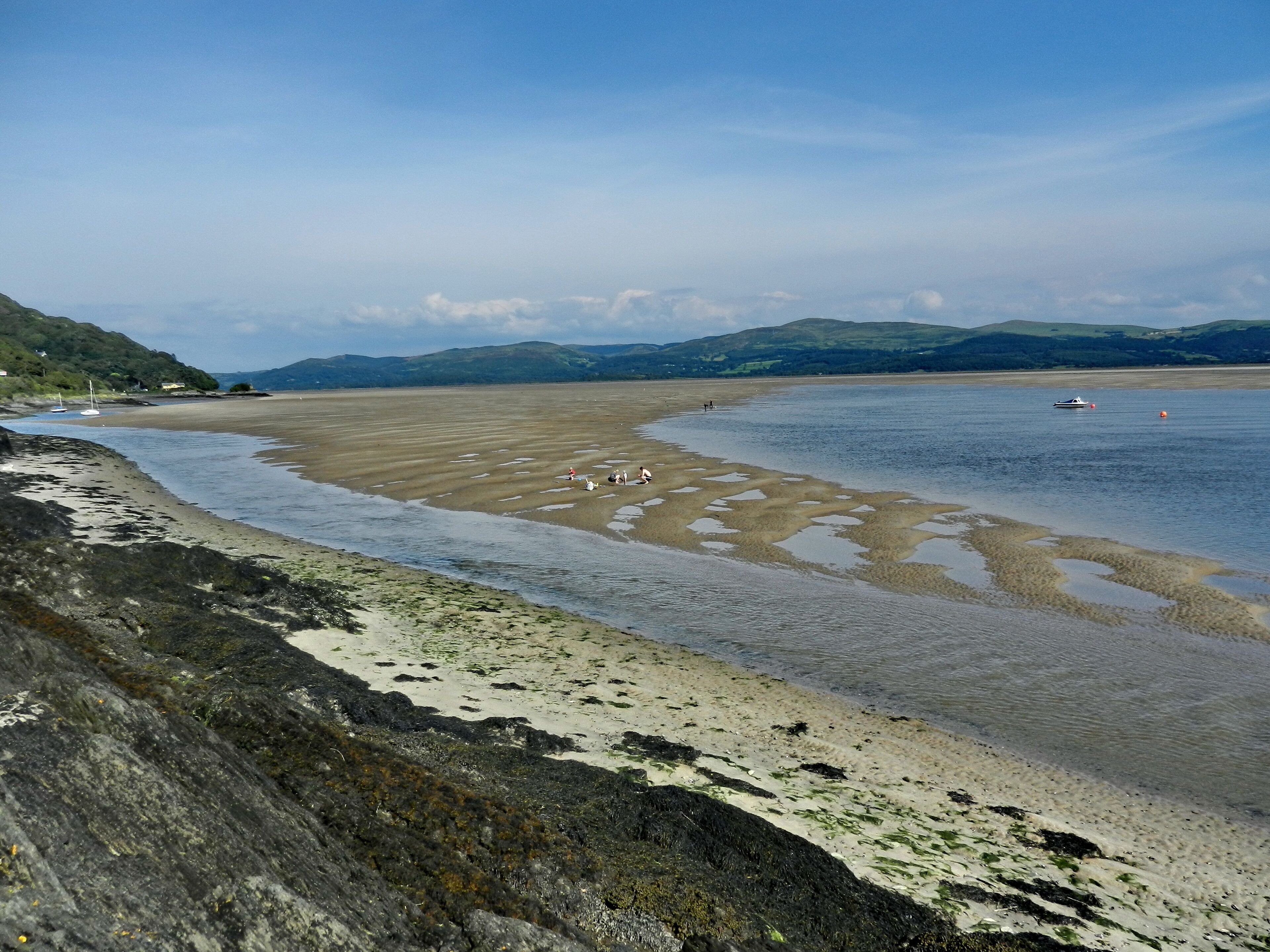 A coastal landscape with a sandy beach, rocky shore, and calm water.