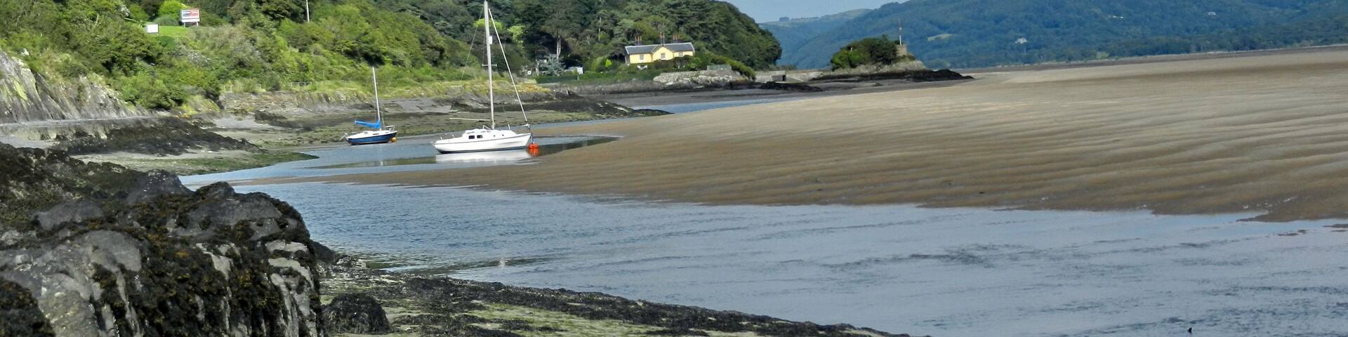 A coastal landscape with a sandy beach, rocky shore, and a sailboat near the shore.