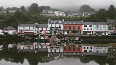 Uma vila costeira com edifícios refletidos em águas calmas, envolta em névoa e vegetação.