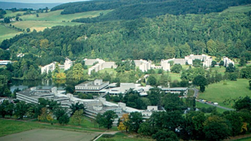 A residential area with multiple apartment buildings surrounded by lush green hills and a lake.