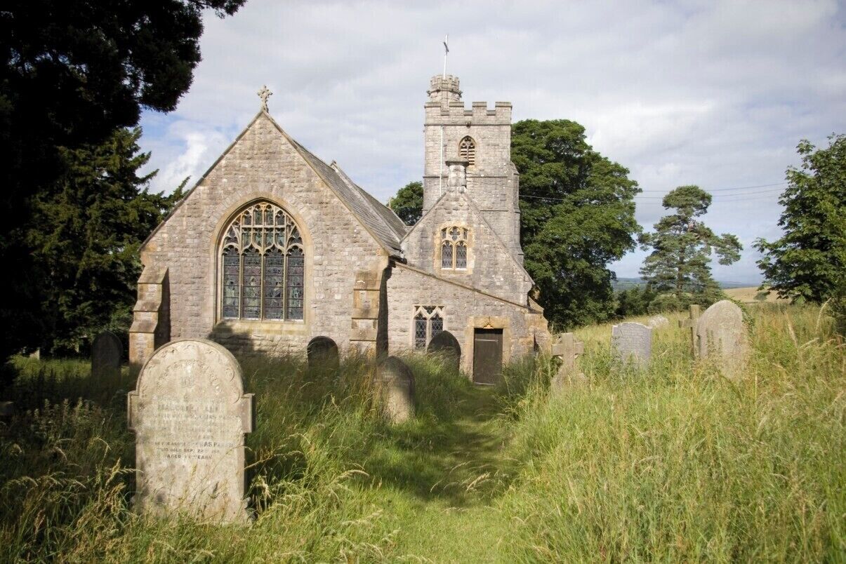 A stone church with a tall tower and arched windows, surrounded by a graveyard with headstones.