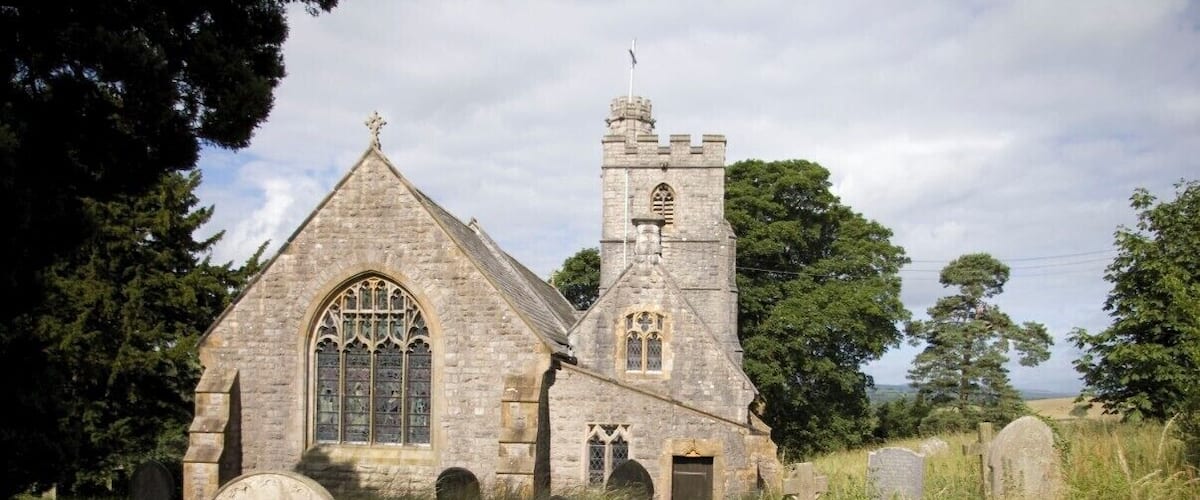 A stone church with a tall tower and arched windows, surrounded by a graveyard with headstones.