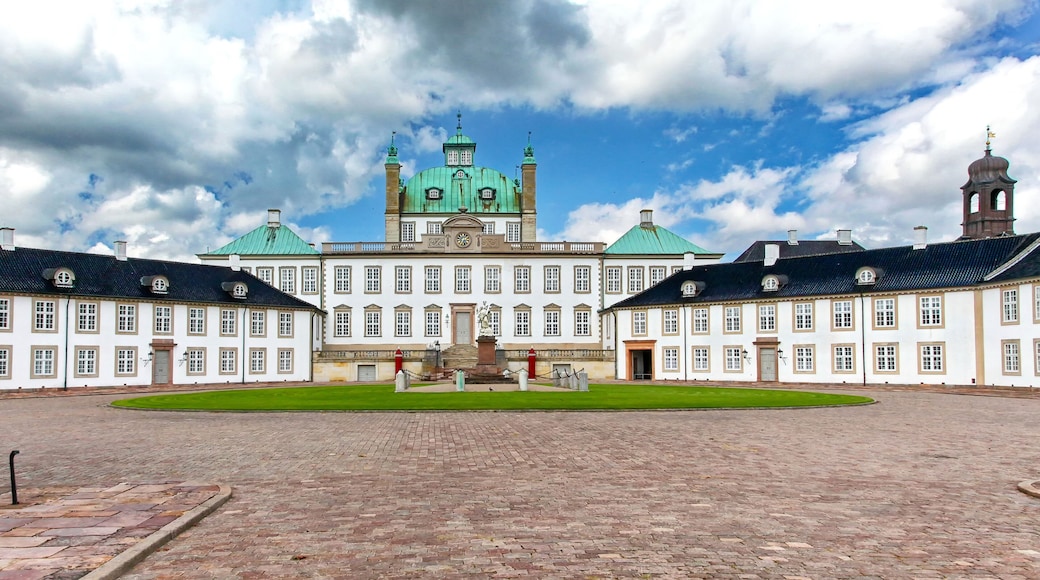 En historisk byggnad med en central, grön kupol, symmetriska flyglar och en innergård med kullerstenar.