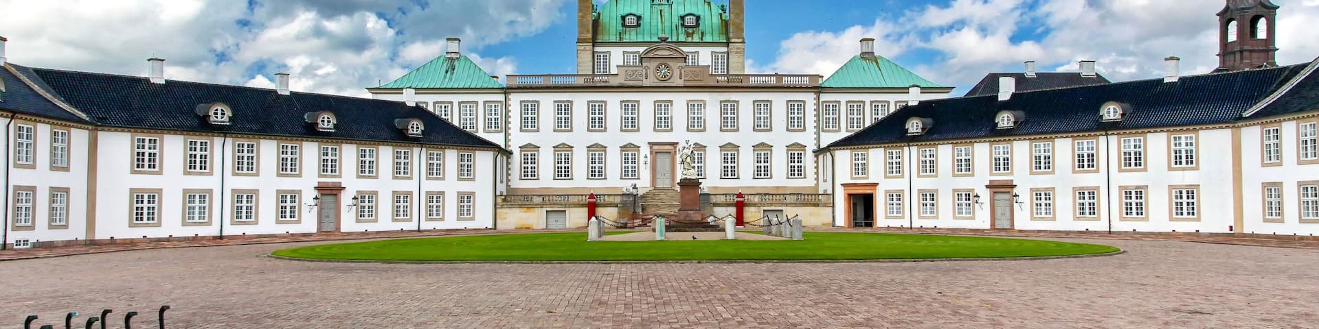 A historic building with a central green dome, symmetrical wings, and a cobblestone courtyard.