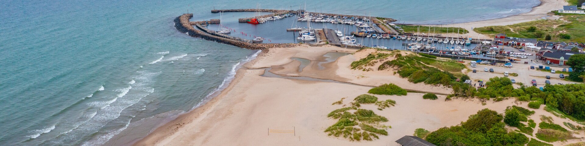 A coastal marina with boats, a sandy beach, and a small building.