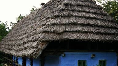 A traditional thatched-roof house with a blue exterior and wooden porch.